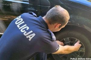 Policjant w mundurze z napisem POLICJA zmienia koło w samochodzie.