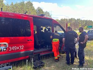 Policjanci i Straż Pożarna stojący przy samochodzie Straży Pożarnej.