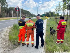 Strażacy i policjant stoją wspólnie i spoglądają na obraz z drona.