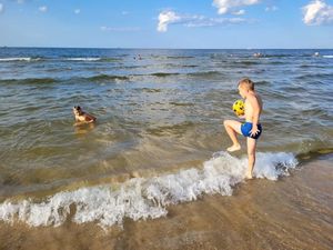 Chłopcy kąpiący się w morzu. Jeden z nich trzyma piłkę.