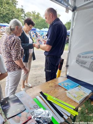 Policjant rozmawiający z dwójką ludzi przed straganem.