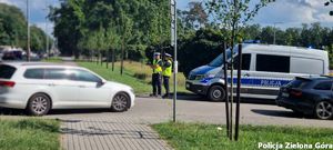 Dwójka policjantów którzy stoją obok radiowozu i patrolują okolice.