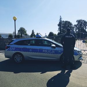 policjant stoi przy radiowozie obok cmentarza.