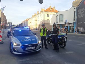 Dwójka policjantów obok radiowozu policyjnego i motocykla.