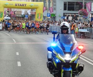 Policjant jadący motocyklem z za nim uczestnicy maratonu.