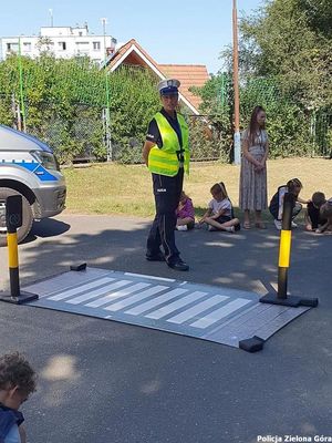 Policjantka przed sztucznymi pasami dla pieszych mówiąca do dzieci.