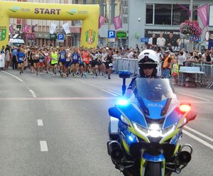 Policjant jadący motocyklem przed dużą grupą biegaczy.