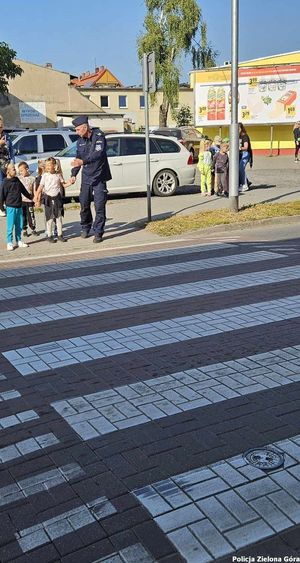 Funkcjonariusz tłumaczy przedszkolakom jak bezpiecznie przejść przez przejście dla pieszych.