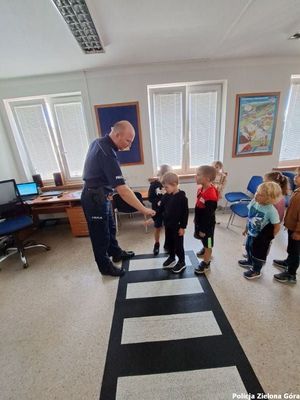 Policjant uczy dzieci jak bezpiecznie przejść przez pasy dla pieszych.