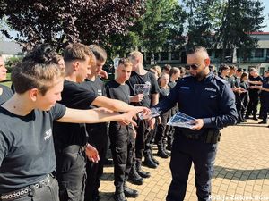 Policjant rozdaje uczniom klasy policyjnej ulotki