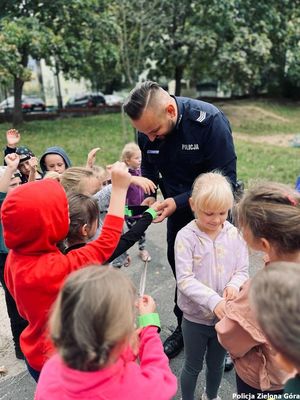 Policjant rozdaje i zakłada dzieciom opaski odblaskowe