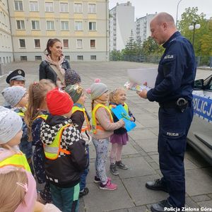 Policjant wręcza dzieciom kolorowe ulotki na temat bezpieczeństwa na drodze