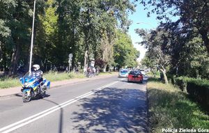 Policjant na motorze i radiowóz zabezpieczają przód rajdu rowerowego