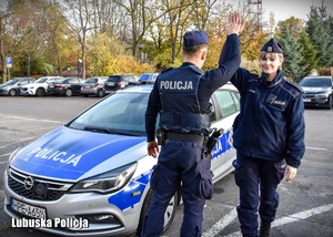 Policjant i policjantka przybijają piątkę przy radiowozie