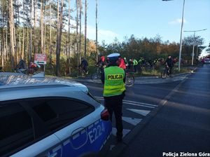 Policjant Ruchu Drogowego stoi przy radiowozie i zabezpiecza trasę rajdu rowerowego