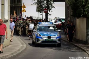 Uroczysty przemarsz prowadzony przez elektryczny radiowóz policji.