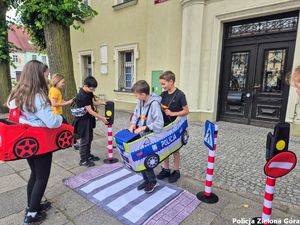 Dzieci przebrane za radiowóz i samochód udają ruch drogowy na przejściu dla pieszych.