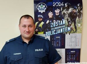 Policjant pozuje na tle kalendarza policyjnego.