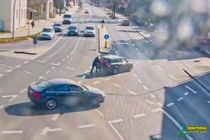 obraz przedstawia umundurowaną policjantkę która pomaga mężczyźnie pchać pojazd na skrzyżowaniu.