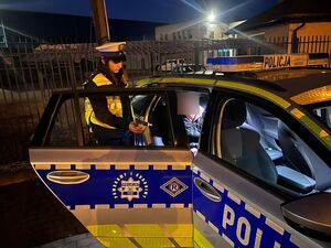 zdjęciu widać umundurowaną policjantkę w białej czapce która wykonuje badanie na zawartość alkoholu kierowcy.