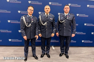 na zdjęciu dwóch policjantów w gabardynie wraz z Komendantem Wojewódzkim Policji w Gorzowie Wielkopolskim w gabardynie. Pozują na ściance do zdjęcia