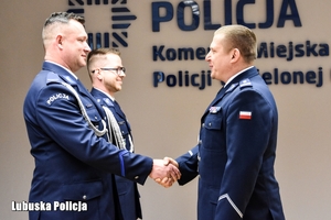 Na zdjeciu widać policjantów w gabardynach wraz z Komendantem Miejskim Policji w Zielonej Górze ubranego również w gabardynę. Komendant gratuluje jednemu z policjantów uściskiem dłoni.