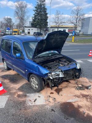 Zdjęcie przedstawia niebieski samochód osobowy po zderzeniu z motocyklem. Przód auta jest pogięty, uszkodzony, maska pogięta, uniesiona.
