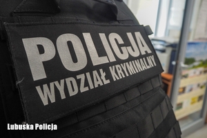 zdjęcie przedstawia część pleców z ubraną czarną kamizelką taktyczną z napisem: Policja wydział kryminalny.
