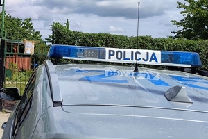 zdjęcie przedstawia bulaje policyjnego radiowozu na tle bramy wejściowej na ogródki działkowe